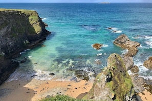 Eine Küstenlandschaft mit sandigem Strand, steinernen Felsen und klarem, blauem Wasser.