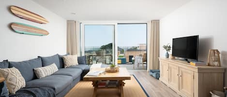 A modern living room with a sofa, coffee table, TV, and a balcony with outdoor furniture.