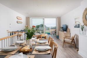Ein Essbereich mit einem Tisch für vier Personen, einem Fernseher auf einem Schrank und Blick auf einen Balkon mit einem Pool.