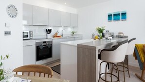 Cocina moderna con armarios blancos, horno empotrado, microondas y una zona de bar con taburetes.