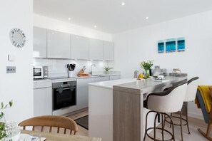 Eine moderne Küche mit weißen Schränken, einem eingebauten Backofen, einer Mikrowelle und einer Theke mit Hockern.