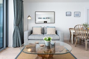 Ein modernes Wohnzimmer mit einem grauen Sofa, einem Glastisch und einem Essbereich mit einem Holzstuhl.