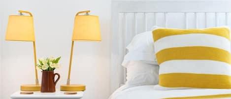 A bed with white and yellow striped bedding, a nightstand with two lamps, and a vase with flowers.