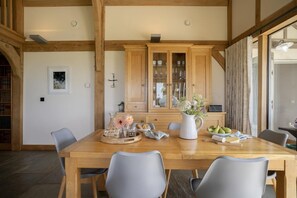 Un coin repas comprenant une table en bois, des chaises grises, un meuble avec des portes en verre et un vase rempli de fleurs.