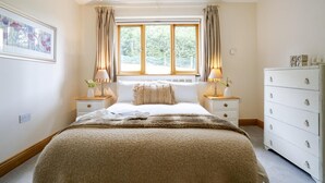 A bedroom with a large bed, two bedside tables with lamps, a dresser, and a window with curtains. - 3 Bed in Widemouth Bay (oc-b581851) (Rosecare)