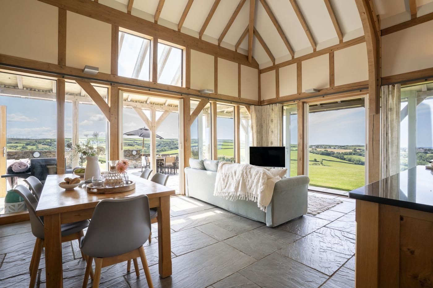 A spacious room with a high ceiling, wooden beams, a dining area with a table and chairs, a sofa, and a television.