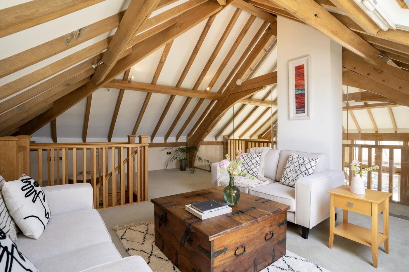A loft-style room with a sloped ceiling, wooden beams, a white sofa, a wooden coffee table, and a small wooden side table.