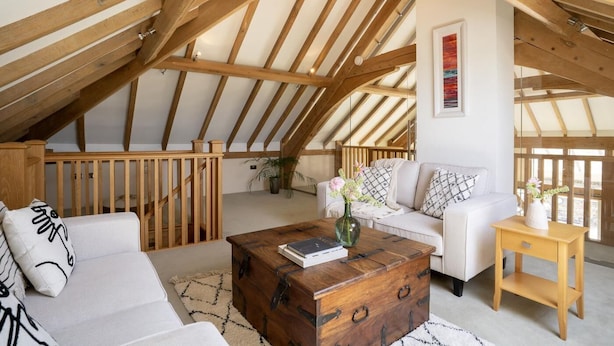 A loft-style room with a sloped ceiling, wooden beams, a white sofa, a wooden coffee table, and a small wooden side table. - 3 Bed in Widemouth Bay (oc-b581851) (Rosecare)