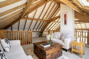 A loft-style room with a sloped ceiling, wooden beams, a white sofa, a wooden coffee table, and a small wooden side table. - 3 Bed in Widemouth Bay (oc-b581851) (Rosecare)
