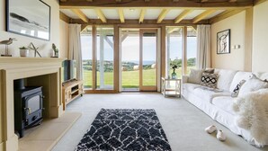 A cozy living room with a fireplace, a sofa, and a view of the countryside. - 3 Bed in Widemouth Bay (oc-b581851) (Rosecare)