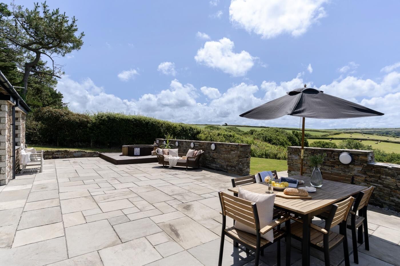 Eine Terrasse im Freien mit Steinböden, einem Holztisch mit Stühlen, einer Couch und einem Sonnenschirm.