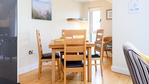 A dining area with a wooden table and chairs, a painting on the wall, and a clock. - 2 Bed in Porth (oc-b584286) (Newquay)