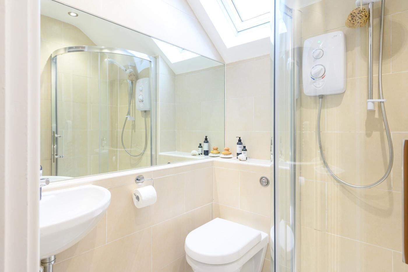 Ein modernes Badezimmer mit Dachfenster, einer gläsernen Duschkabine, einer Toilette und einem Waschbecken.