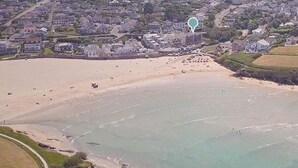 An aerial view of a coastal area with a beach, residential buildings, and a road. - 2 Bed in Porth (oc-b584286) (Newquay)