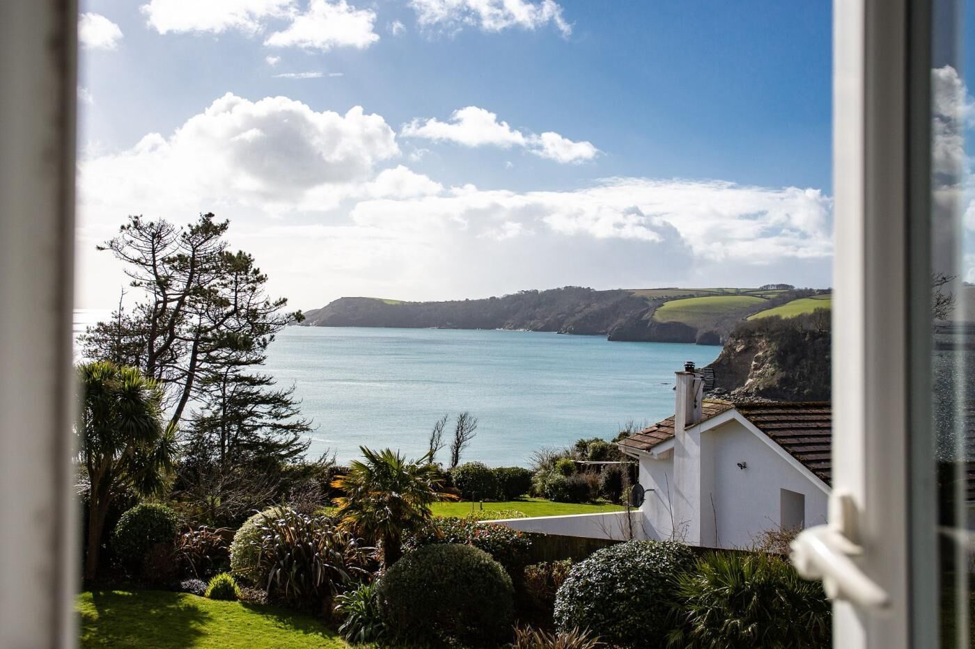 A coastal view with a clear sky, a body of water, and a white building with a garden in the foreground.