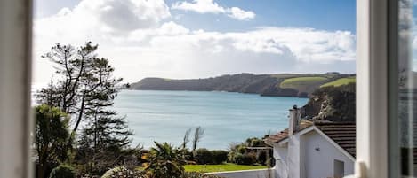 A coastal view with a clear sky, a body of water, and a white building with a garden in the foreground.