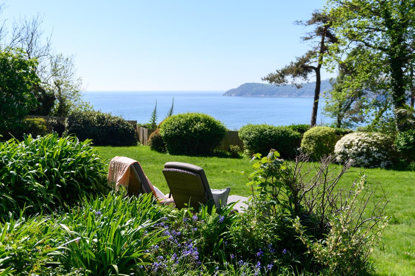 A garden with a lawn, two chairs, and a view of the sea.