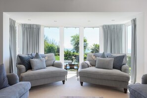 A modern living room with two grey sofas, a coffee table, and a view of a lush garden through large windows. - 4 Bed in Charlestown (oc-b610558) (Charlestown)