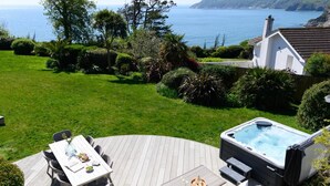 En terrass med ett bubbelbad, ett bord med stolar och utsikt över havet.
