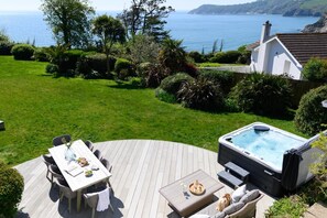 A deck with a hot tub, a table with chairs, and a view of the sea. - 4 Bed in Charlestown (oc-b610558) (Charlestown)