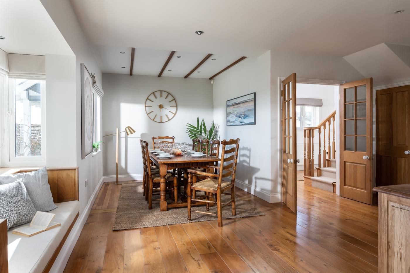 A dining area with a wooden table, chairs, a clock, and a painting on the wall.