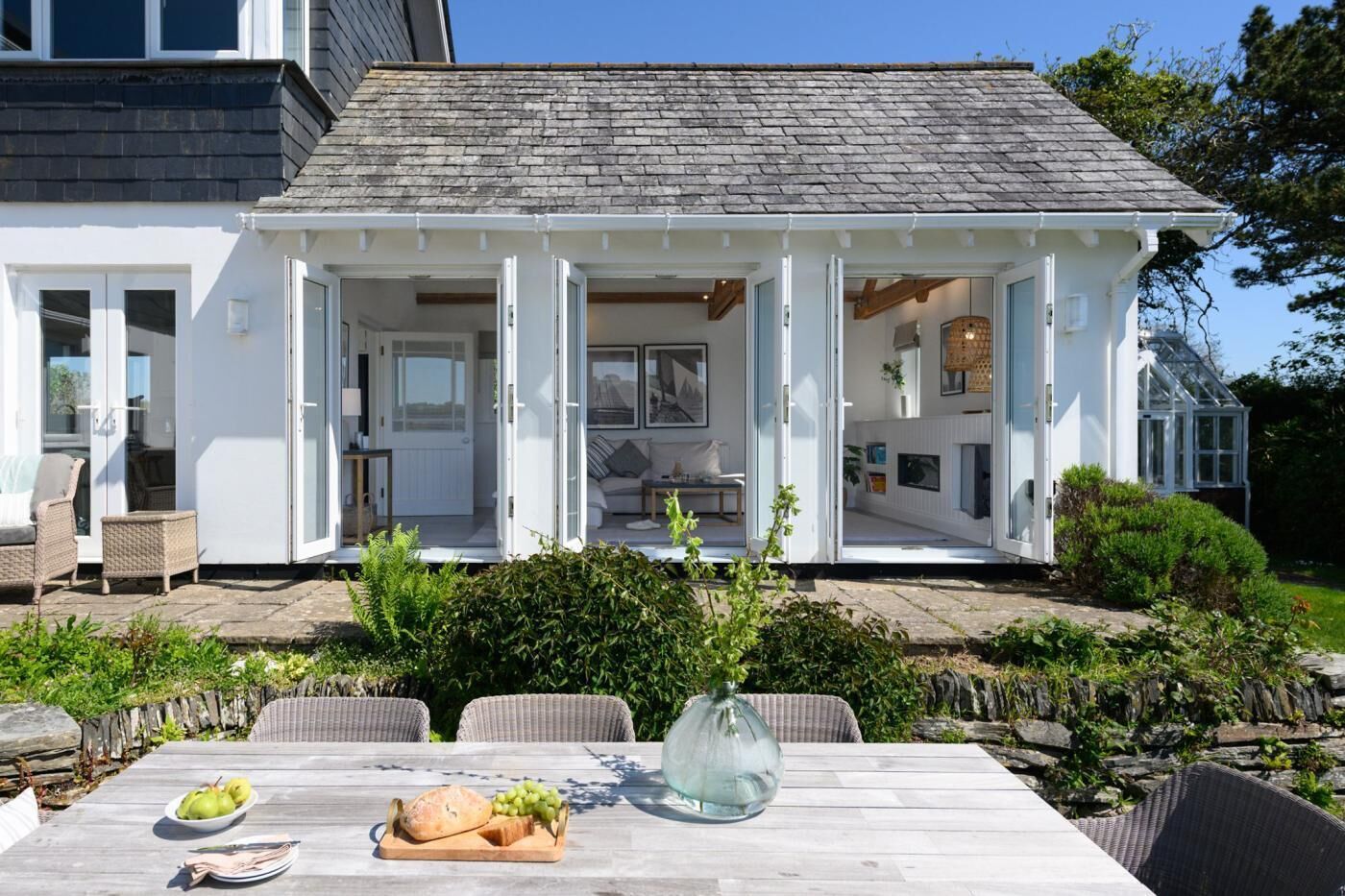 A white house with a covered patio, outdoor seating, and a table with food.