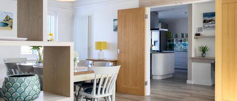 A modern kitchen with white cabinets, a dining area with a white table and chairs, and a wooden floor.