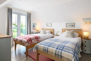 Een tweepersoonskamer met twee bedden, een houten bureau, een rood-wit geruit tapijt en uitzicht op groen door het raam.