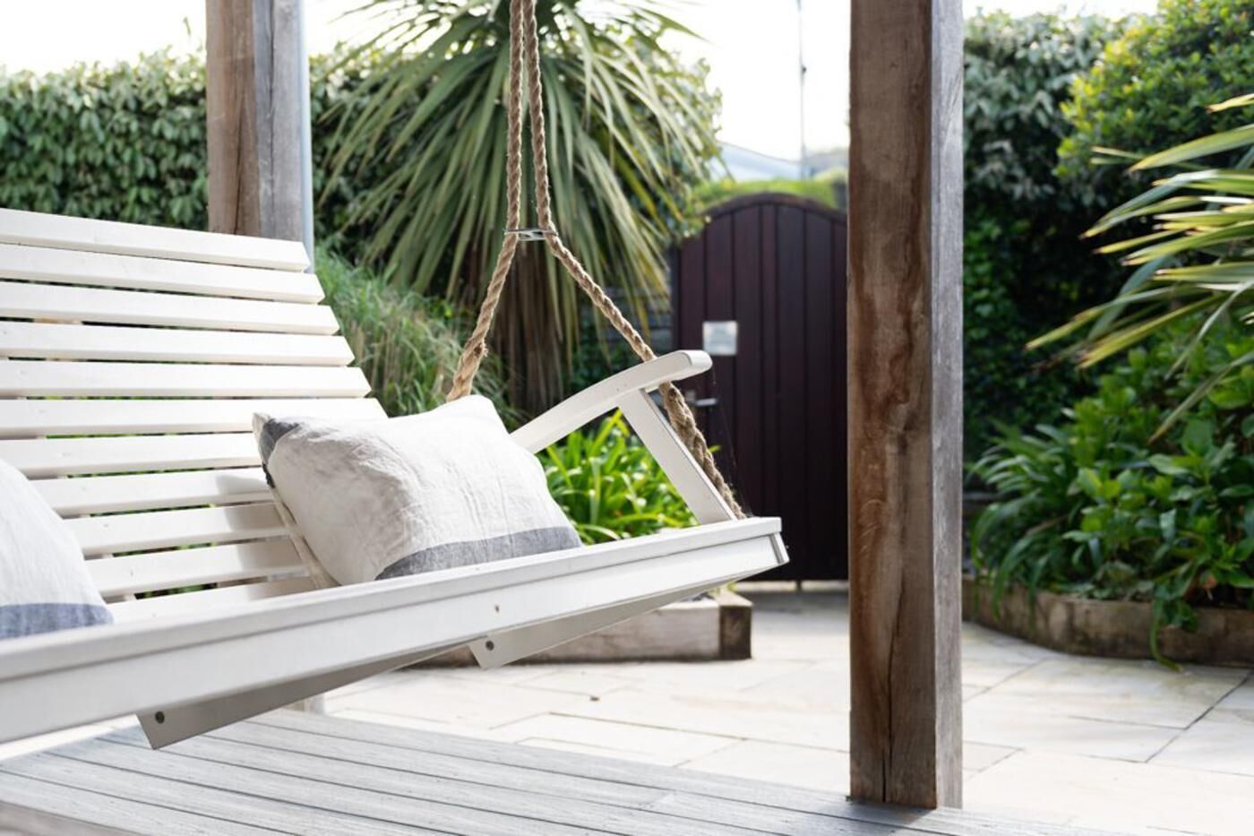 A white outdoor bench with cushions, a rope swing, and a wooden post structure.