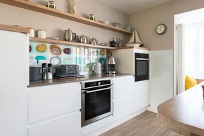 A compact kitchen with white cabinets, a built-in oven, and a coffee maker. - 4 Bed in Trevone (oc-b637403) (Trevone)