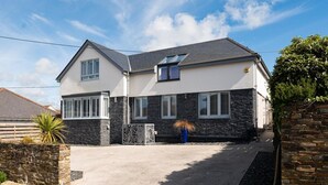 A two-story house with a stone facade, a driveway, and a clear sky. - 4 Bed in Trevone (oc-b637403) (Trevone)
