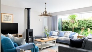 A modern living room with a fireplace, a sofa set, a television, and a view of greenery outside. - 4 Bed in Trevone (oc-b637403) (Trevone)