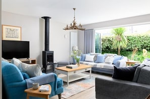 Ein modernes Wohnzimmer mit Kamin, einer Sofagarnitur, einem Fernseher und Blick auf Grünflächen.