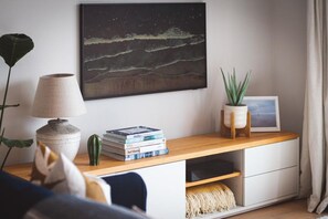 Un salon moderne avec une console en bois, une lampe, une plante, un tableau encadré et une œuvre d’art accrochée au mur.