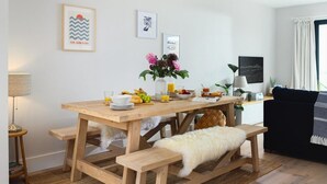 Een eetgedeelte met een houten tafel gedekt voor het ontbijt, een bankje en een bank op de achtergrond.