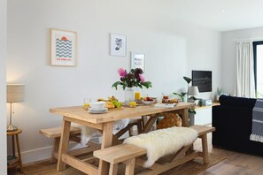 Ein Essbereich mit einem Holztisch, gedeckt für das Frühstück, einer Bank und einer Couch im Hintergrund.