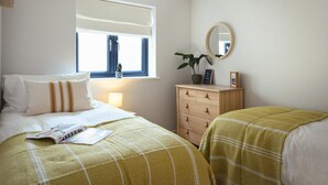 Een slaapkamer met een bed, nachtkastje, kapstok, raam en een spiegel.