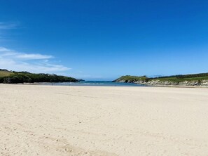 Ein weiter Sandstrand mit sanften Hängen zu beiden Seiten, die zum Meer hinabführen.