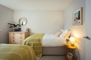 Une chambre à coucher avec un lit, une table de chevet avec une lampe, une commode, un miroir et un tableau encadré accroché au mur.