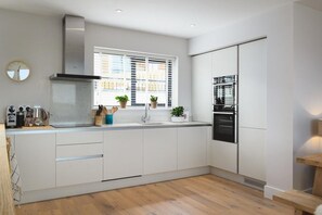 Eine moderne Küche mit weißen Schränken, einem Backofen und einem Fenster mit Jalousien.