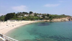 Ein Küstenstrand mit klarem Wasser, einem Sandufer und Häusern an einem Hügelhang.