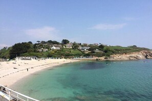 A coastal beach with clear waters, a sandy shore, and houses on a hillside. - 4 Bed in Falmouth (oc-b588809) (Goldenbank)