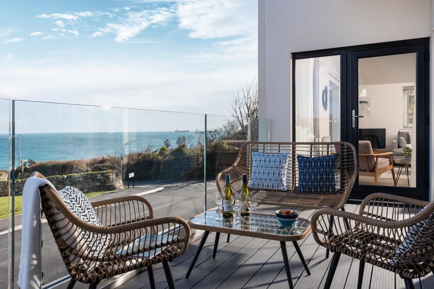 A balcony with wicker furniture, a glass table, and a view of the sea.