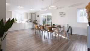 Eine moderne Küche mit weißen Schränken, einem Esstisch mit Stühlen und einem großen Fenster, das für natürliches Licht sorgt.