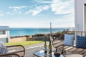 A balcony with wicker furniture, a glass table, and bottles of wine. - 4 Bed in Falmouth (oc-b588809) (Goldenbank)
