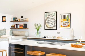 Eine moderne Küche mit einer zentralen Kochinsel, einem Essbereich mit einer Couch und einem Bücherregal mit Büchern.