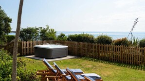 A hot tub in a backyard with a wooden fence, a grassy area, and a view of the sea. - 4 Bed in The Lizard (oc-b620048) (Coverack)