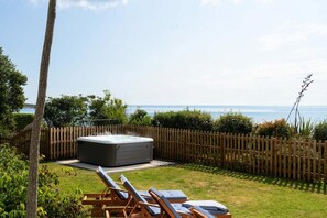 A hot tub in a backyard with a wooden fence, a grassy area, and a view of the sea. - 4 Bed in The Lizard (oc-b620048) (Coverack)
