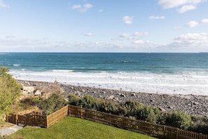 A coastal view with a rocky beach, a wooden fence, and a grassy area. - 4 Bed in The Lizard (oc-b620048) (Coverack)
