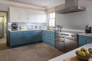 A kitchen with blue cabinets, a stainless steel stove, and a window with blinds. - 4 Bed in The Lizard (oc-b620048) (Coverack)